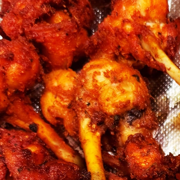 Close-up of several crispy, red-orange Indian chicken lollipops with visible bones.