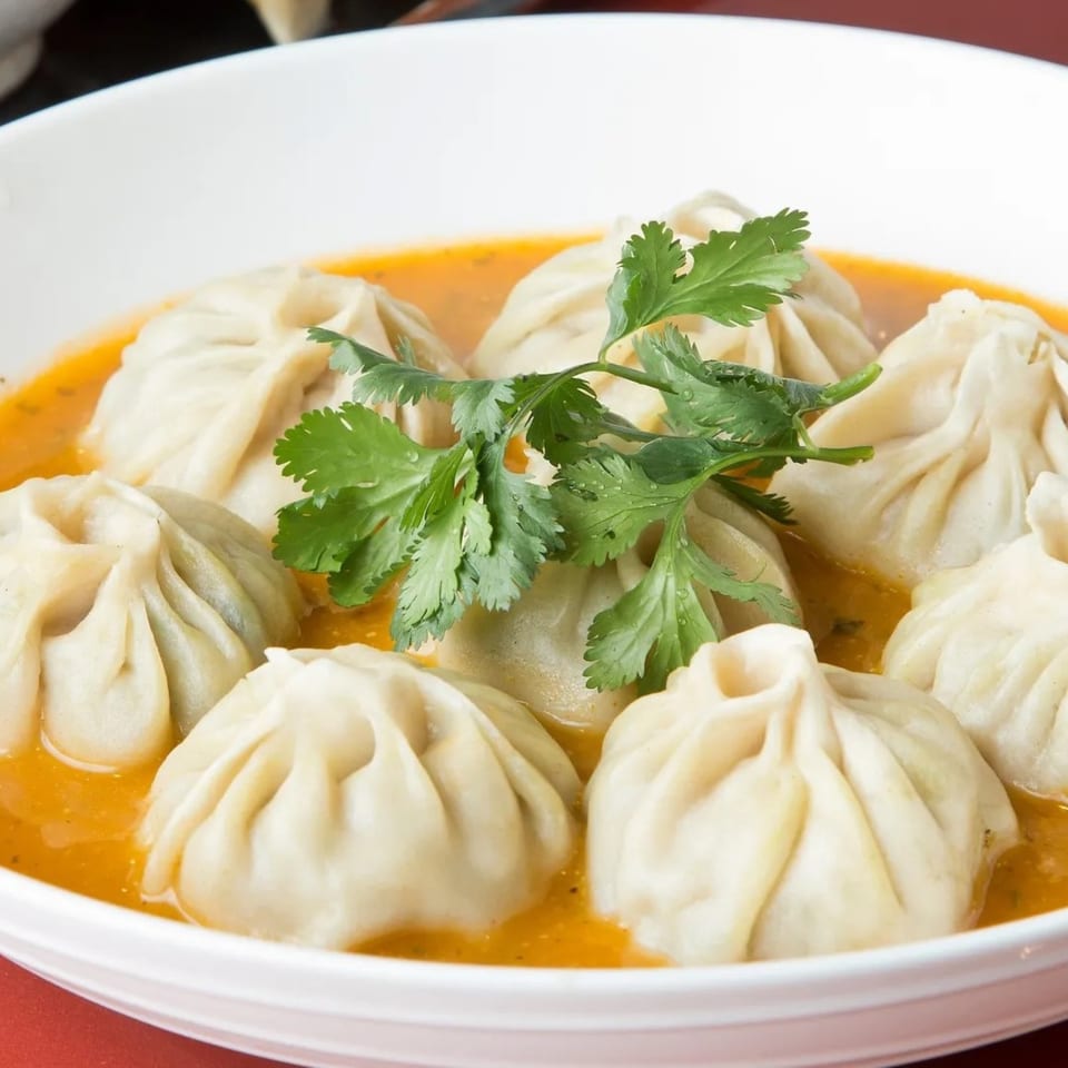 CURRYZONE's Indian momos, steamed dumplings in a rich orange sauce, garnished with fresh cilantro.