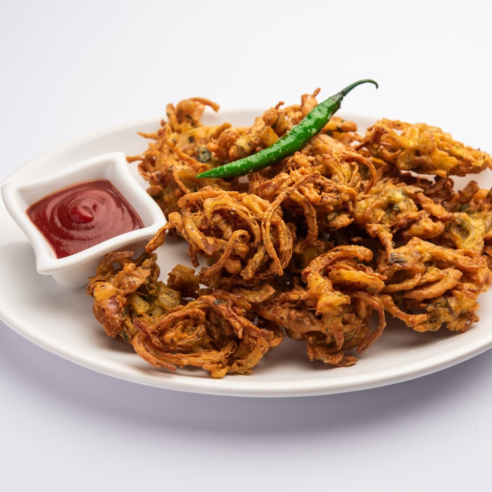 Crispy Indian onion pakoras with a side of ketchup and a green chili on a white plate.