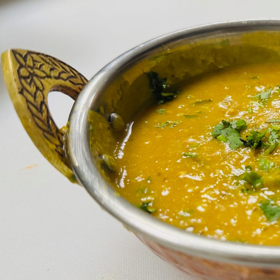 Close-up of a golden Indian curry, garnished with fresh cilantro, in a metal bowl with an ornate handle.