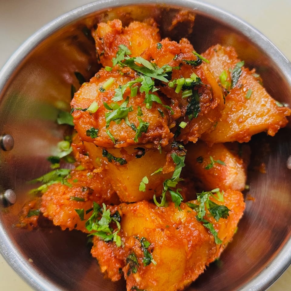 Indian aloo gobi, potato and cauliflower curry, garnished with fresh cilantro in a metal bowl.