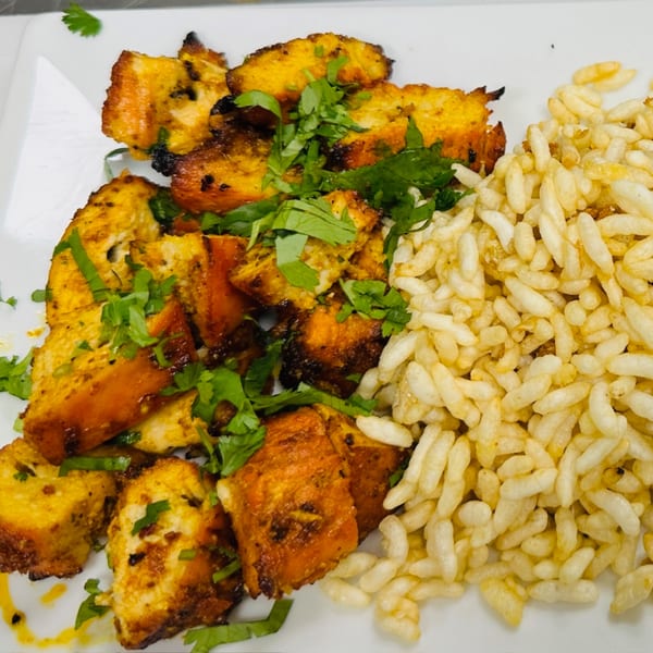 CURRYZONE's Indian chicken tikka, garnished with fresh cilantro, served with puffed rice on a white plate.