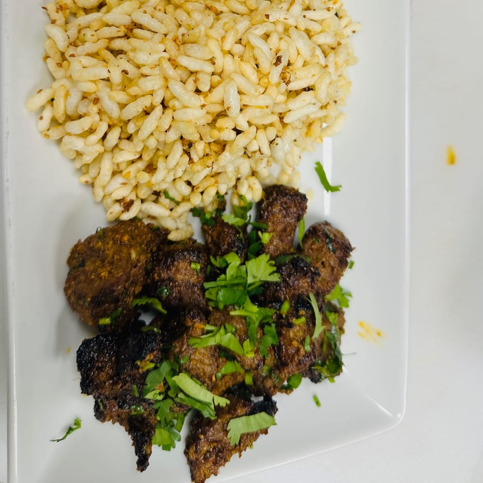 CURRYZONE's Indian dish with dark spiced meat pieces garnished with cilantro and a side of puffed rice.