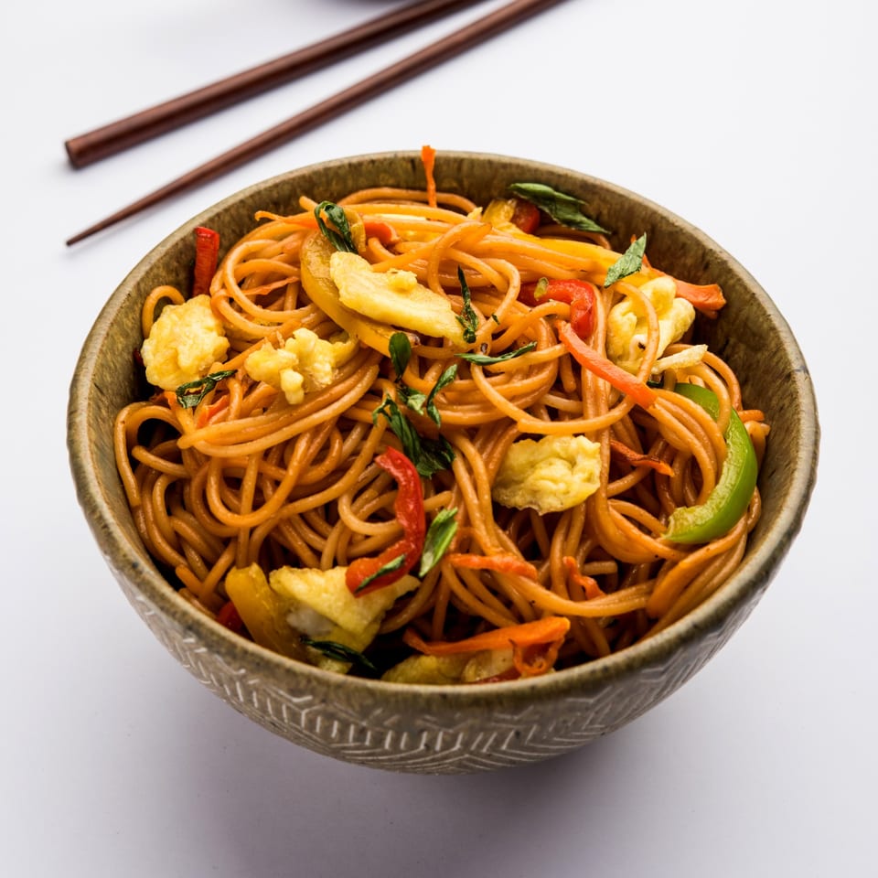 A bowl of CURRYZONE's Indian-style noodles with vegetables and scrambled egg, with chopsticks in the background.