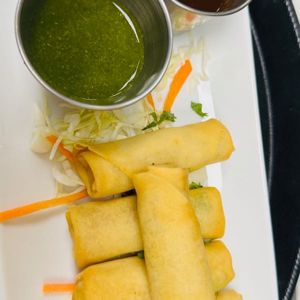 Golden spring rolls with shredded cabbage, carrots, and two dipping sauces on a white plate.